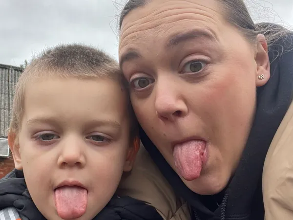 A woman and her son are close together, both sticking their tongues out for the camera.