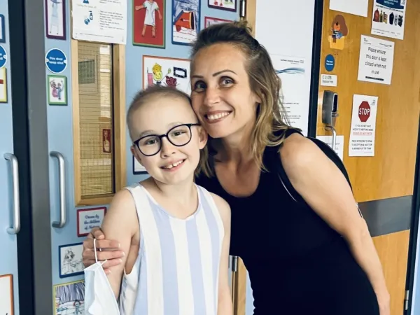 A mother has her arm around her daughter, who has little hair in the hospital.