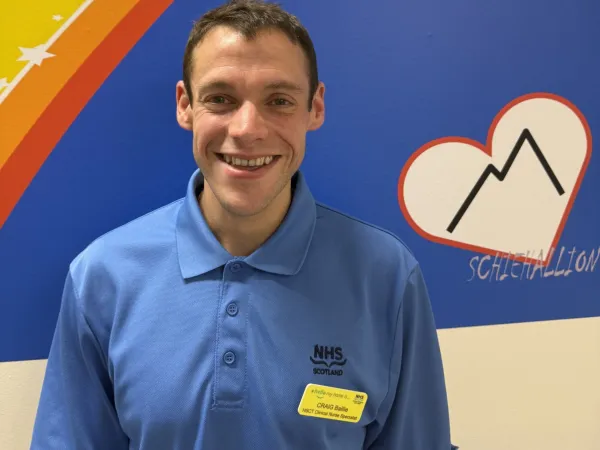 A man in a blue NHS Scotland uniform smiling at the camera.