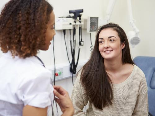 A young woman sitting in an examination room smiling and talking to a doctor