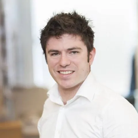 Johnathan smiling at the camera. He has dark hair and is wearing a white shirt. 