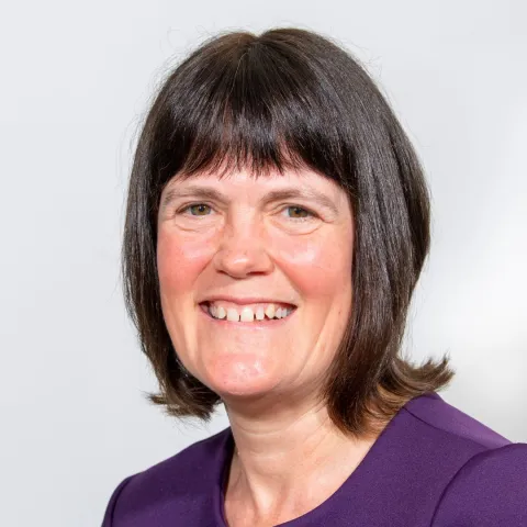 Chris smiling at the camera with short dark hair and wearing a purple top.