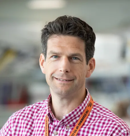 Matthew smiling at the camera with short dark hair and a red checked shirt.