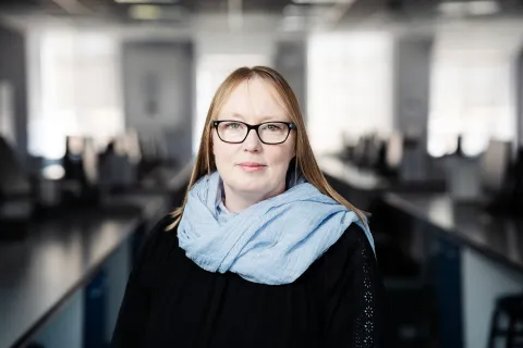 Suzanne smiling at the camera with straight blonde hair, wearing a blue scarf and black top.