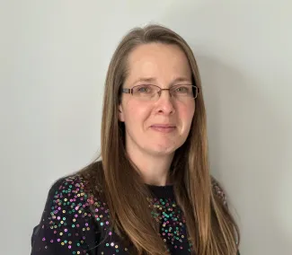A headshot of a woman with dark long hair and glasses