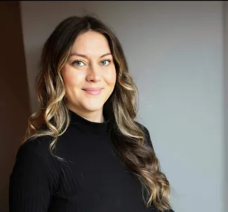 A headshot of a woman with long dark hair, smiling while wearing a black shirt.  