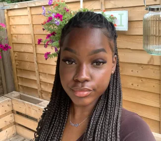 A young woman with dark, braided hair is smiling as she takes a selfie in the garden.