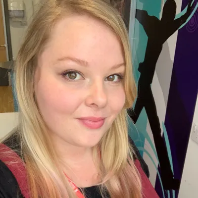 Lois smiling at the camera with long blonde hair and wearing burgundy dungarees.