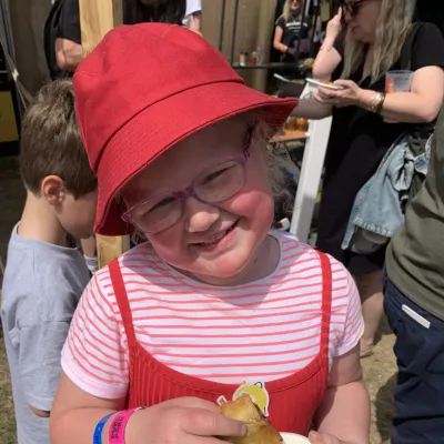 Annika wearing a red hat and dress, smiling at the camera while holding food.