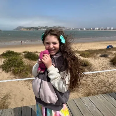 Lila with long dark hair, smiling at the beach.