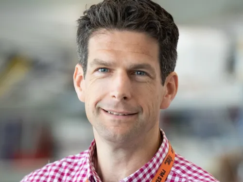 Matthew smiling at the camera with short dark hair and a red checked shirt.