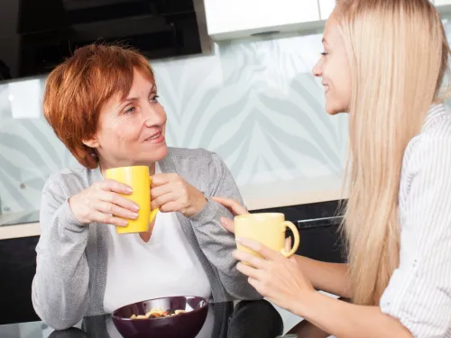 A young woman is sitting talking to her mother over a cup of coffee.
