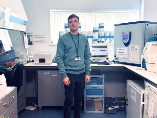 Dr Nick Jones stood in a lab, wearing a jumper and lanyard.