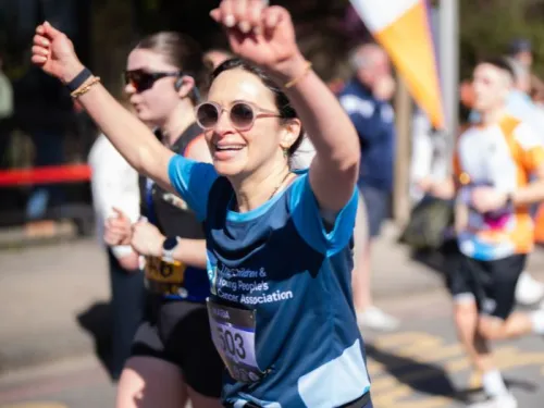 A smiling runner with her hands in the air, running the London Landmarks Marathon with a CCLG top